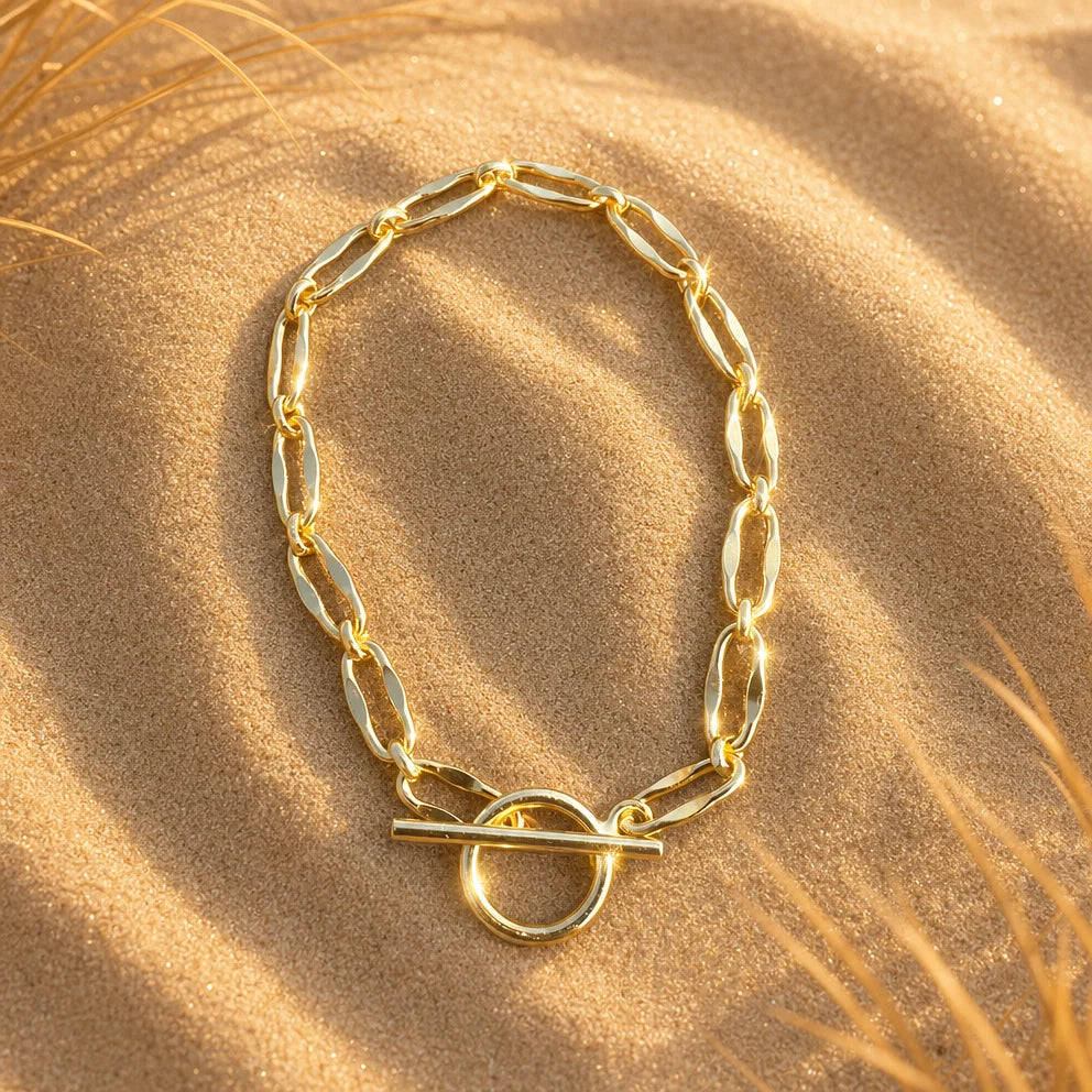 Flat lay of Frequency Paris-Ibiza Burning Desire gold T-bar bracelet on golden sand