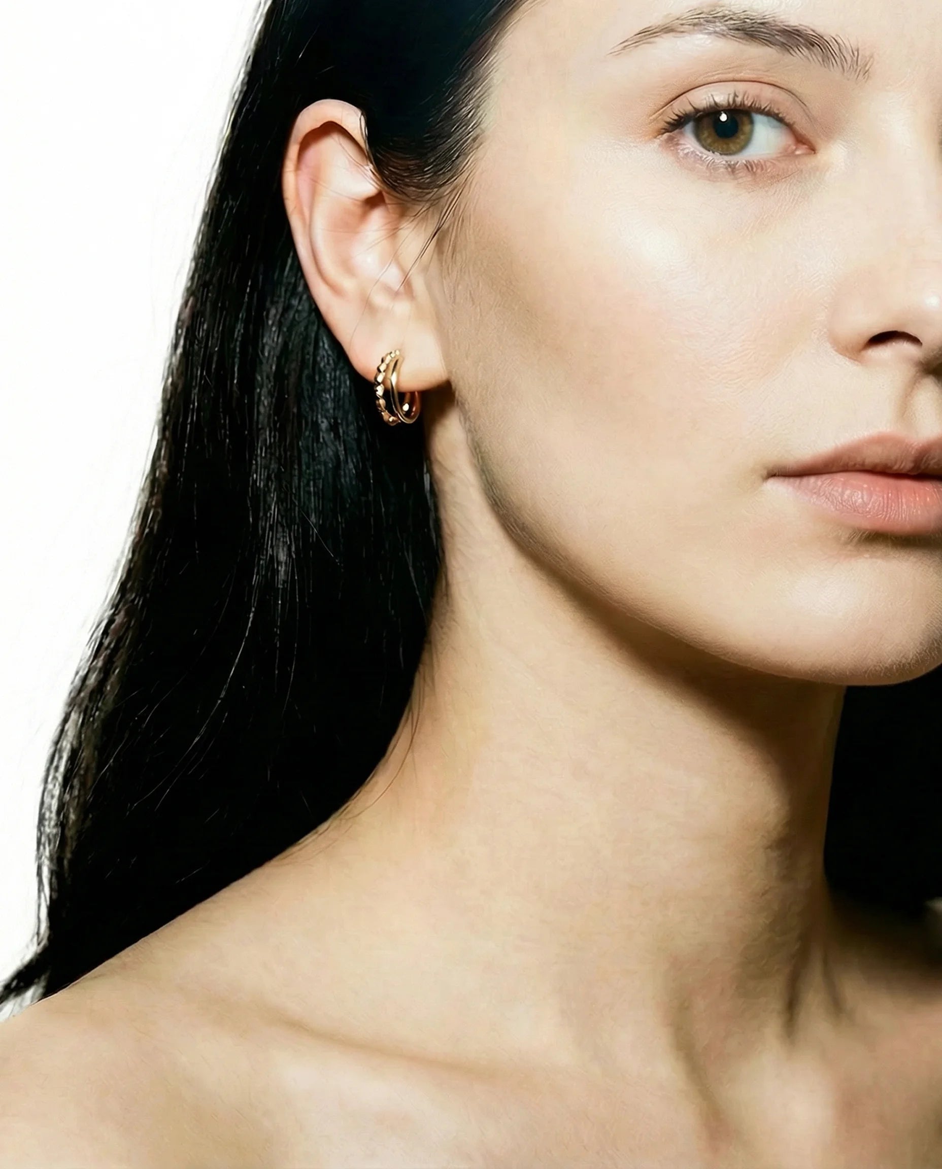 Model wearing Frequency Paris-Ibiza Divine Feminine Gold Hoop Earrings. Two-hoop illusion design in 18K gold-plated sterling silver, delicate, eye-catching, and versatile for everyday or special occasions.