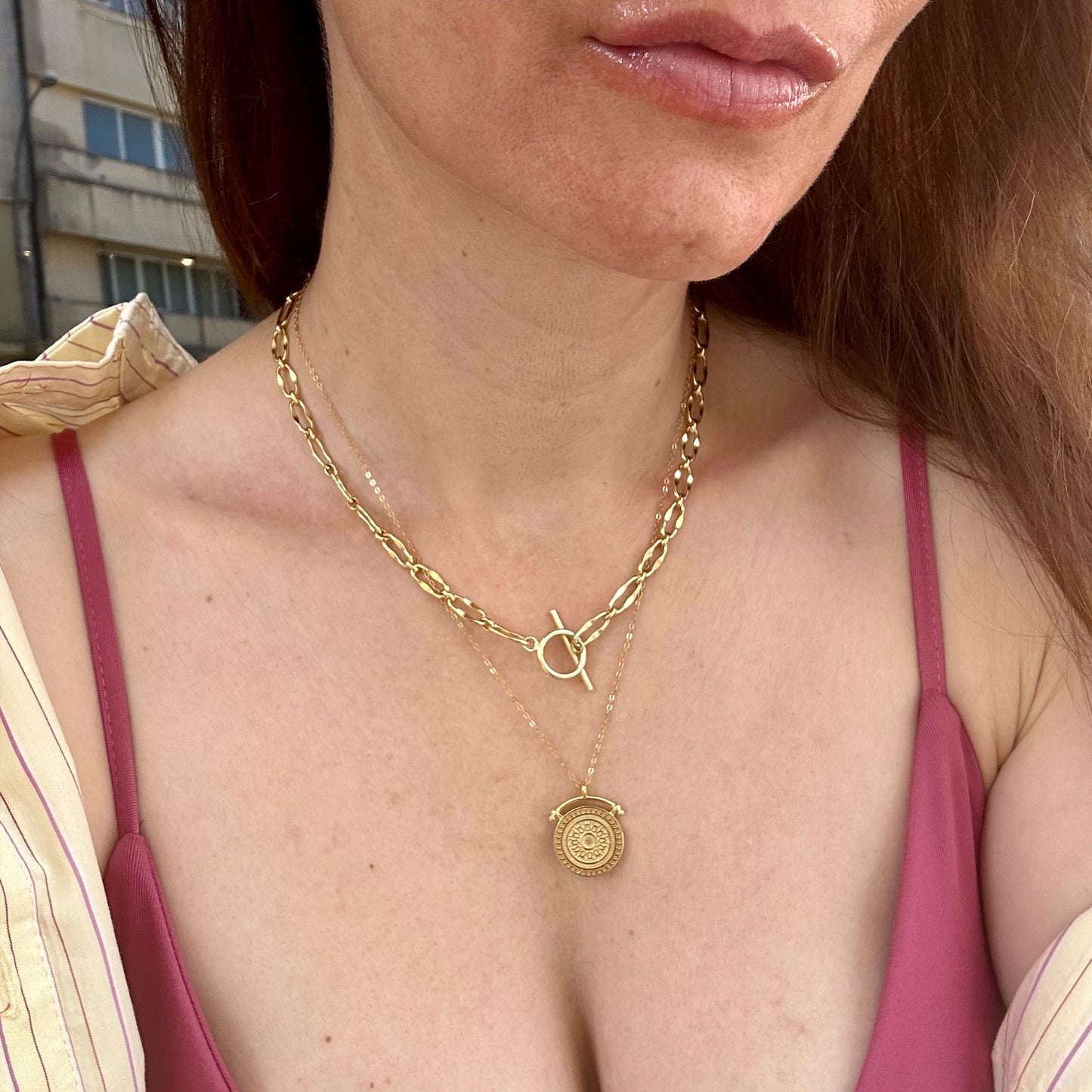 Close-up of Sunbeam Gold Pendant Necklace 18K gold plated on model wearing crisp yellow shirt and pink bodice, layered with 18K Gold Burning Desire Chain necklace, showcasing luxe layering style. Frequency-Paris-Ibiza