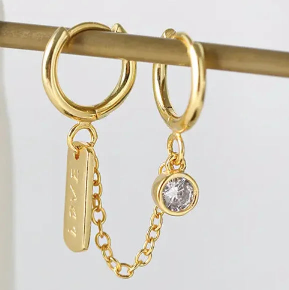 Close-up of Frequency Paris-Ibiza Self Love Huggie Chain Earrings in gold-plated sterling silver. Showcasing double huggie design, chain link, crystal drop gemstone, and ‘love’ tag. Excellent craftsmanship.