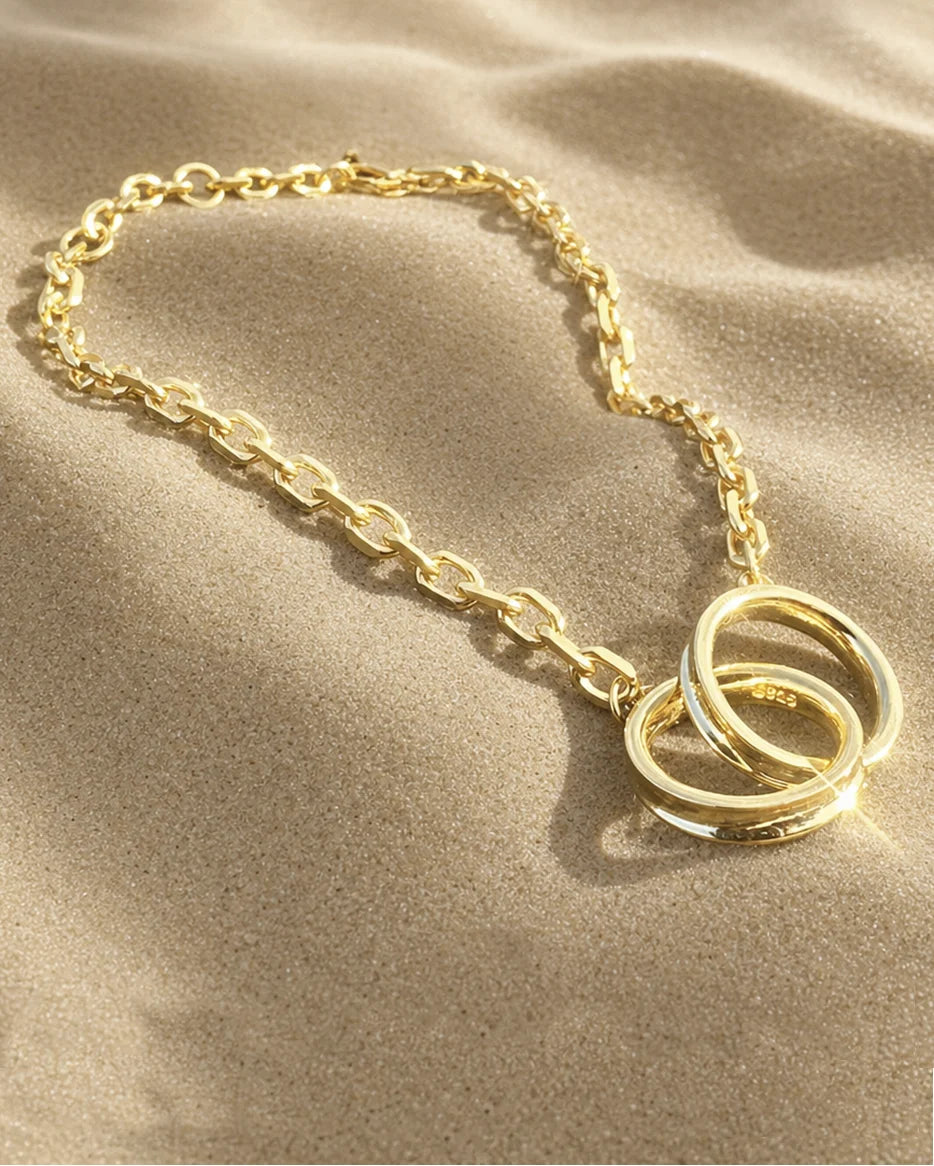 Close-up of Frequency Paris-Ibiza Infinite Possibilities Gold Chain Bracelet showing interlocking circle detail against textured  golden sand