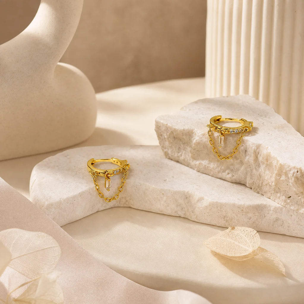 Close-up of Frequency Paris-Ibiza Infinity Huggie Earrings with clear zircon crystals, detailed crystal huggies, center drop crystal, and delicate chain hoop design in 18k gold-plated sterling silver.