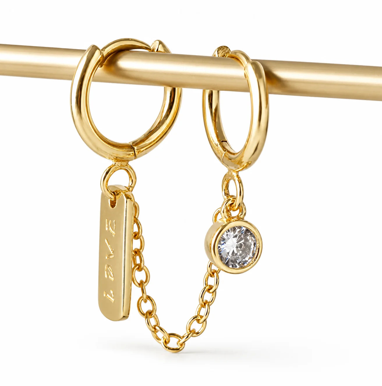 Close-up of Frequency Paris-Ibiza Self Love Huggie Chain Earrings in gold-plated sterling silver. Showcasing double huggie design, chain link, crystal drop gemstone, and ‘love’ tag. Excellent craftsmanship.