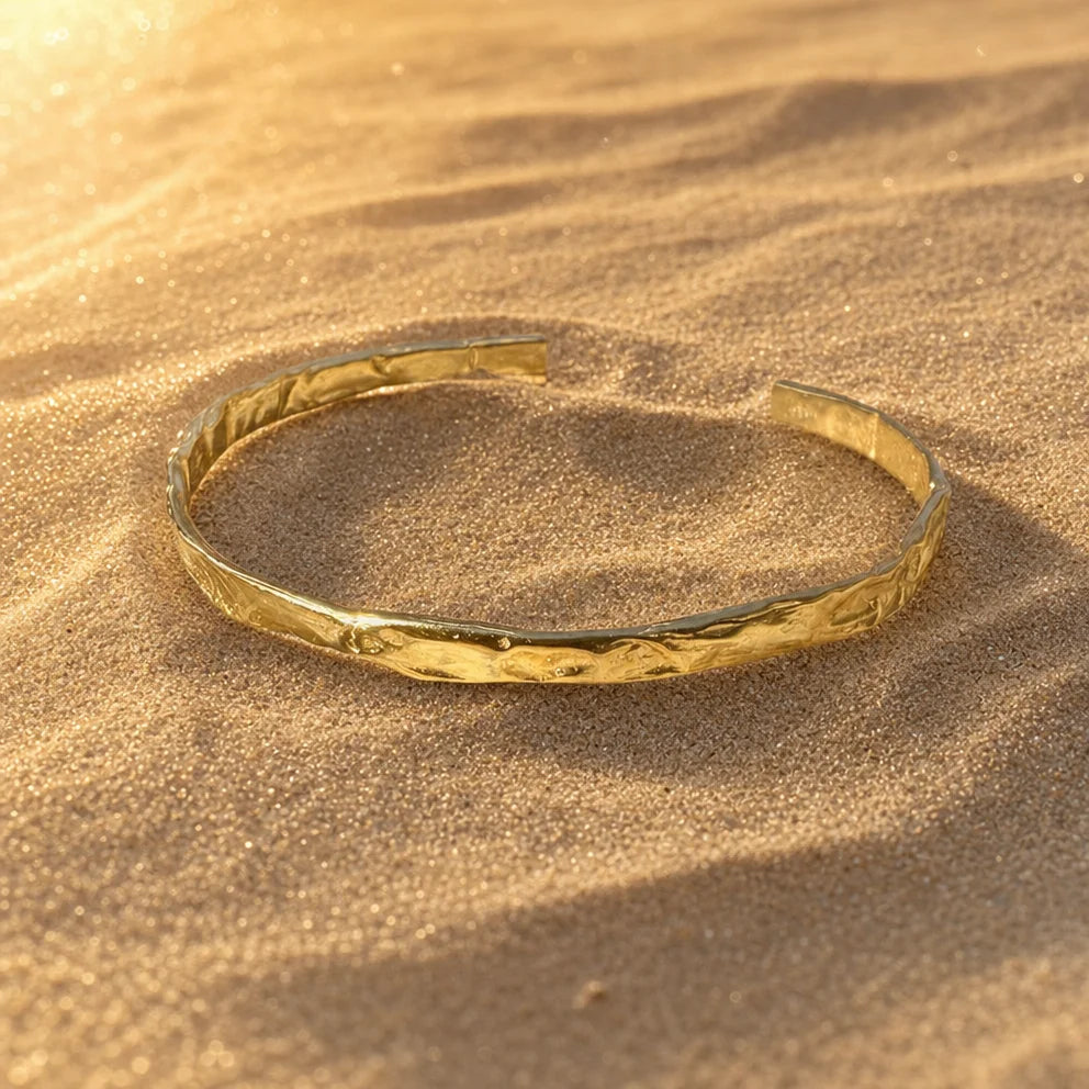 Close-up of Frequency Paris-Ibiza So Hum gold cuff bracelet showing hammered texture and craftsmanship on natural rocks
