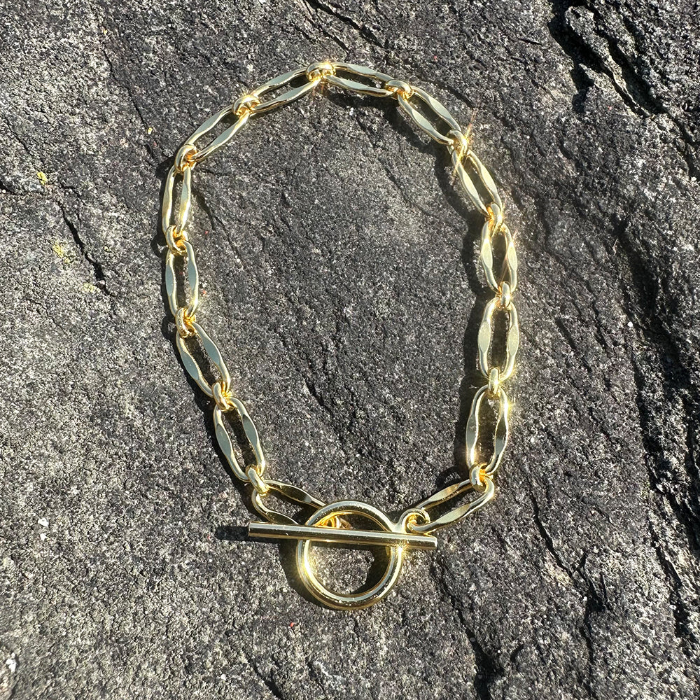 Flat lay of Frequency Paris-Ibiza Burning Desire gold T-bar bracelet on grey rocks