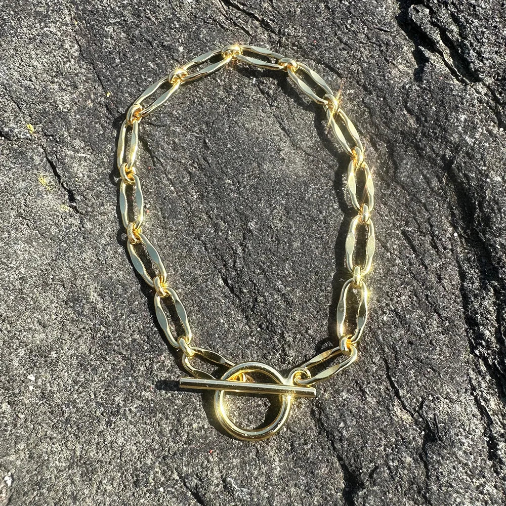 Flat lay of Frequency Paris-Ibiza Burning Desire gold T-bar bracelet on grey rocks