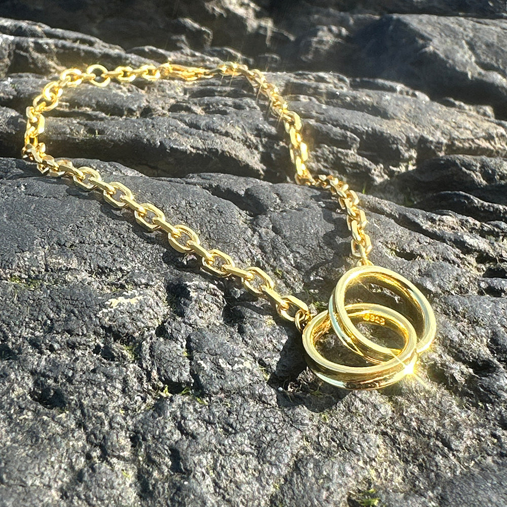 Close-up of Frequency Paris-Ibiza Infinite Possibilities Gold Chain Bracelet showing interlocking circle detail against textured grey rocks