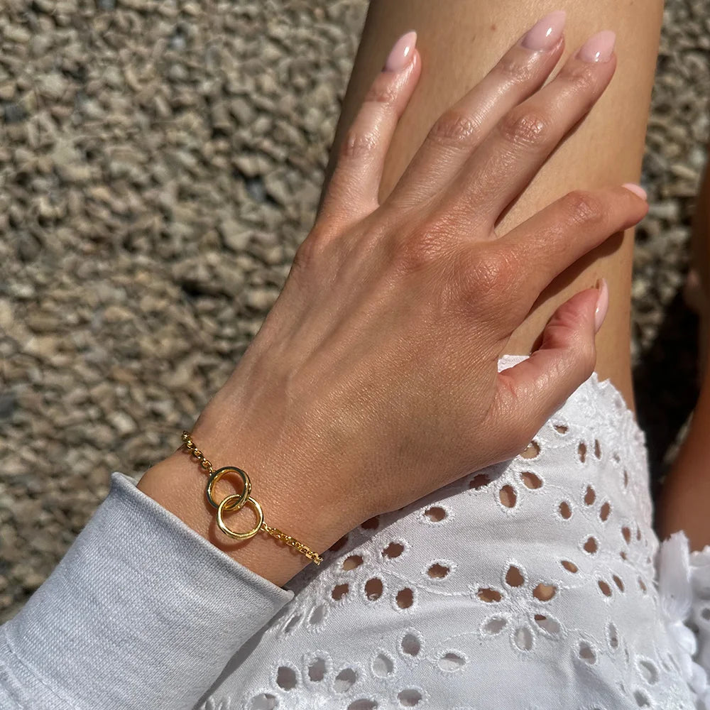 Frequency Paris-Ibiza Infinite Possibilities Gold Chain Bracelet worn on wrist, resting on leg at the beach