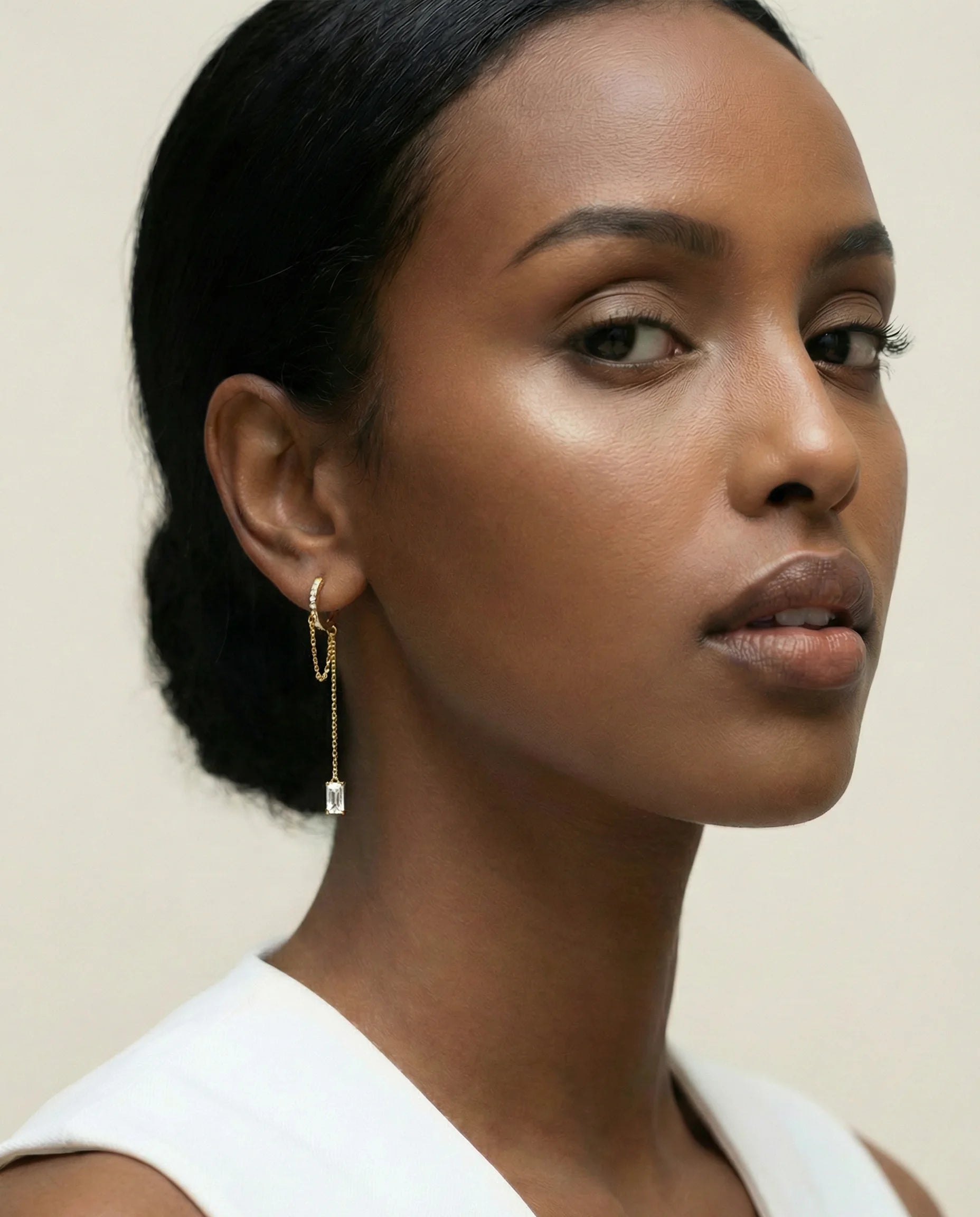 Model wearing Frequency Paris–Ibiza Infinity Chain Earrings in 18K gold, showing embellished crystal huggie and chain drop detail.