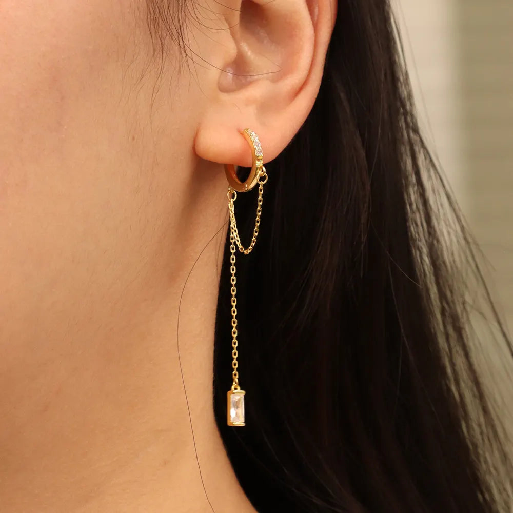 Model wearing Frequency Paris–Ibiza Infinity Chain Earrings in 18K gold, showing embellished crystal huggie and chain drop detail.
