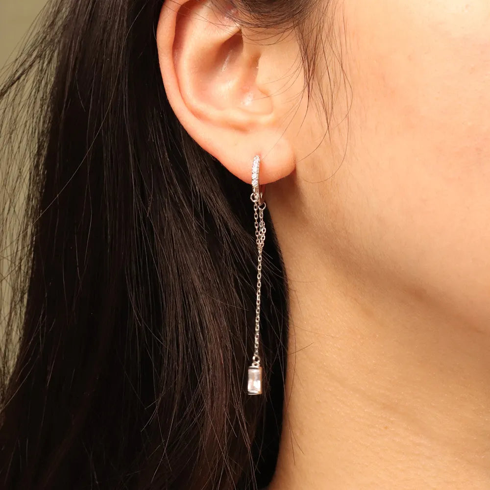 Model wearing Frequency Paris–Ibiza Infinity Chain Earrings in rhodium-plated sterling silver, showing crystal huggie and chain tassel detail.