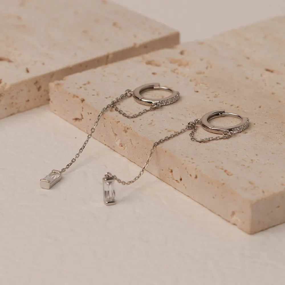 Close-up of Frequency Paris–Ibiza Infinity Chain Earrings in rhodium-plated sterling silver, highlighting crystal drop at the end of chain tassel and exquisite craftsmanship.