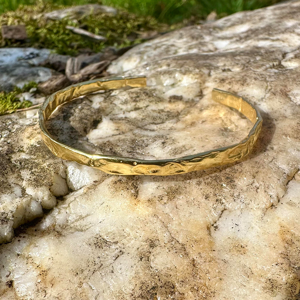 Close-up of Frequency Paris-Ibiza So Hum gold cuff bracelet showing hammered texture and craftsmanship on natural rocks