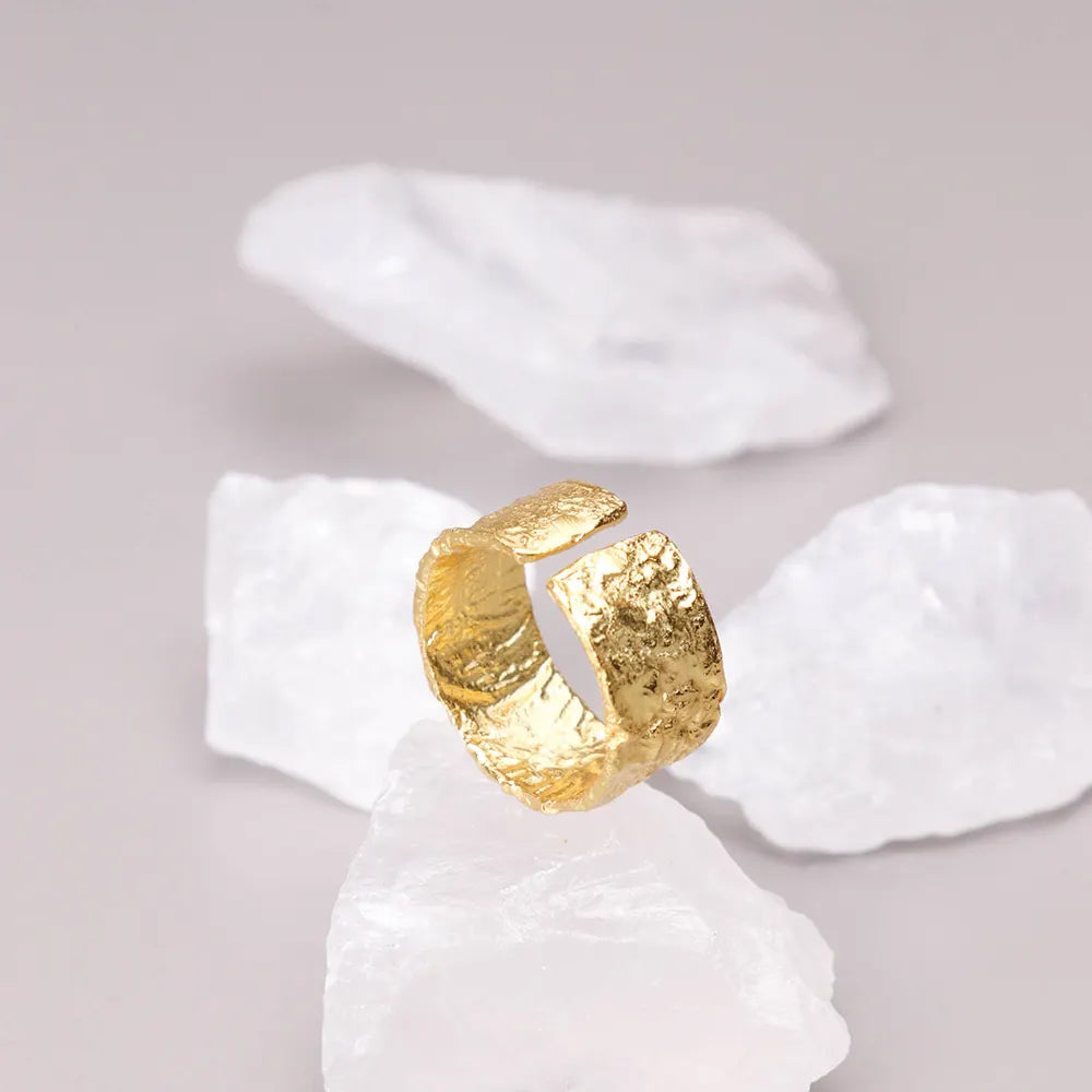 Gaia Ring by Frequency Paris-Ibiza displayed on a bed of crystals, highlighting its adjustable closing and organic hammered texture. The craftsmanship of the 18k gold-plated sterling silver ring exudes both beauty and quality.