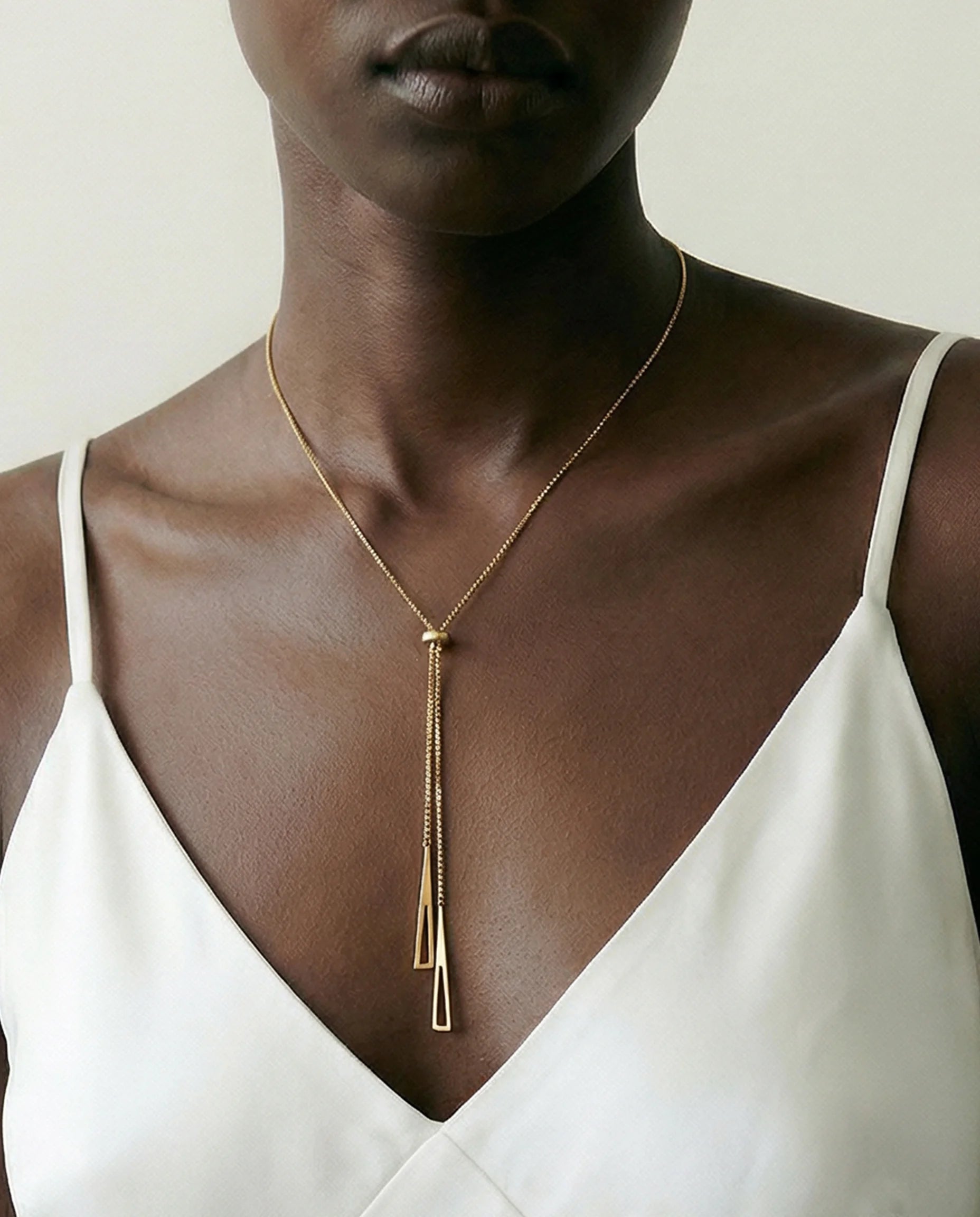 Radiance Gold Chain Necklace close-up on model’s neck styled with a white evening dress— adjustable gold chain with triangle motifs and central bead. Frequency Paris-Ibiza